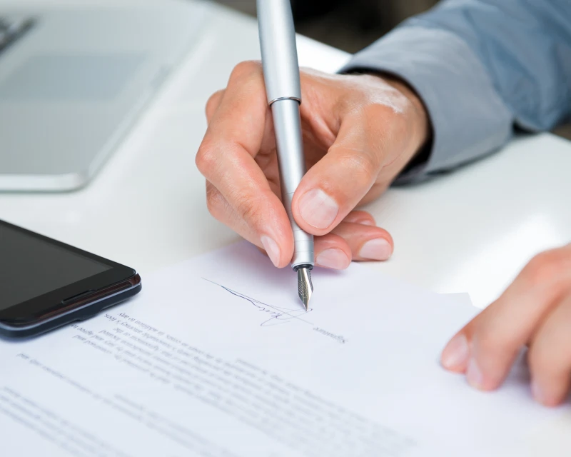 A professional signing a document, representing Greenfields' expert company liquidation services.